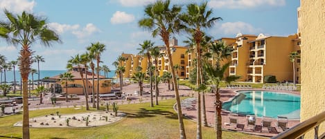 A resort with a pool, palm trees, and a view of the ocean.