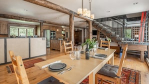 Ein geräumiger Essbereich mit einem Holztisch, gedeckt für vier Personen, umgeben von Holzstühlen. Eine Treppe mit Metallgeländer führt auf eine obere Ebene.