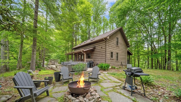 A cabin with a stone fire pit, Adirondack chairs, and a grill.