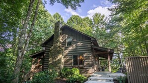 A rustic cabin with a stone chimney, wooden deck, and a covered porch.