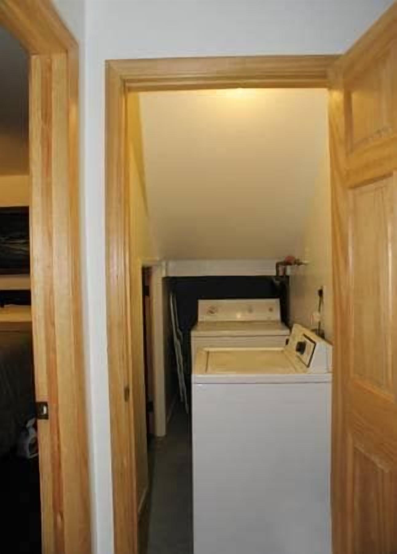 Un cuarto de lavandería con lavadora y secadora, puertas de madera y un pasillo que conduce a otra habitación.