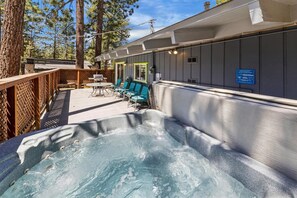 Un espace avec un bain à remous, une terrasse en bois, des sièges extérieurs et une vue sur une zone boisée.