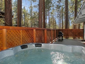 Ein Whirlpool, umgeben von einem Holzzaun, mit Grill und Stühlen im Hintergrund.