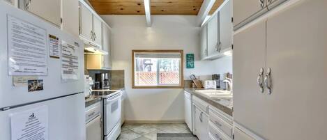 Cocina compacta con armarios blancos, un refrigerador, una ventana y techo de madera.