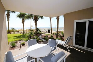 A patio with a white table and chairs, a pool, palm trees, and a view of the ocean. - Sandy Key 122:  2 BR/2 BA Perdido Key, FL Beachfront Condo, On-Site Rental Office, Sleeps 6 (Pensacola)