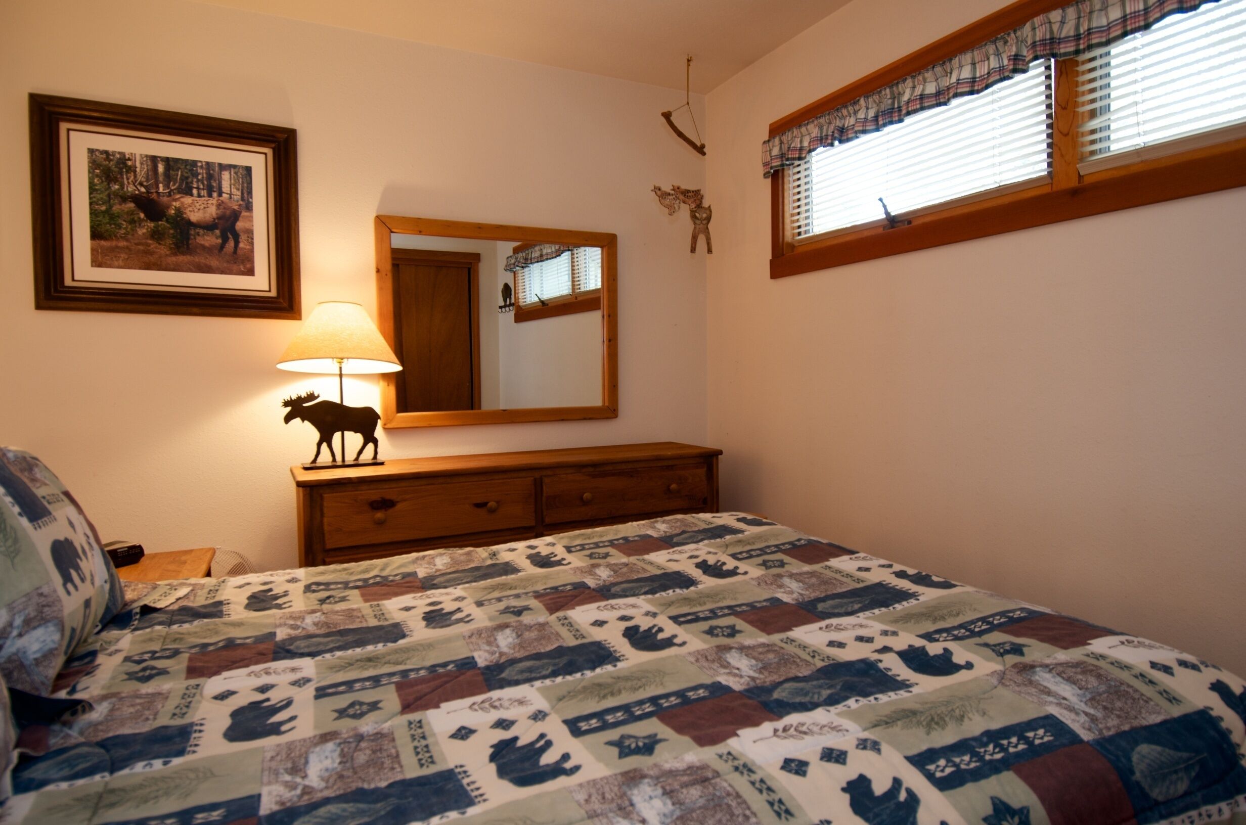 A bedroom with a bed, a dresser, a mirror, and a window with blinds.