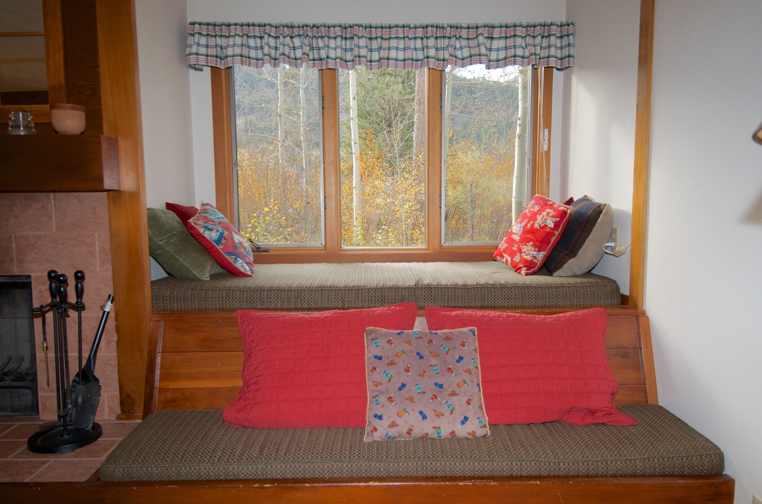 A cozy seating area with a bench and cushions, a fireplace, and a window with a view of trees.
