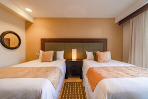 Two single beds with white duvets and throw pillows, a nightstand with a lamp, and a patterned rug.