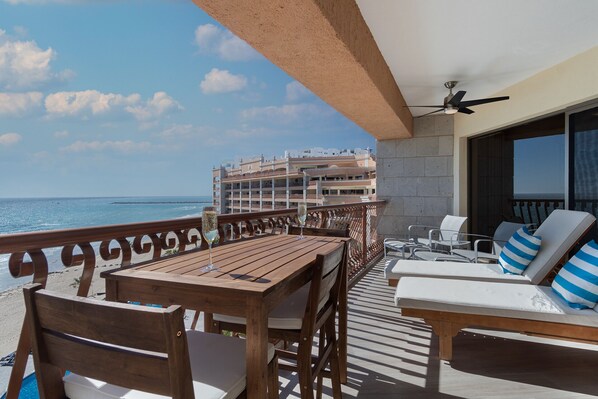 Eine Holzterrasse mit Tisch und Stühlen mit Blick auf einen Strand und ein Hotelgebäude.