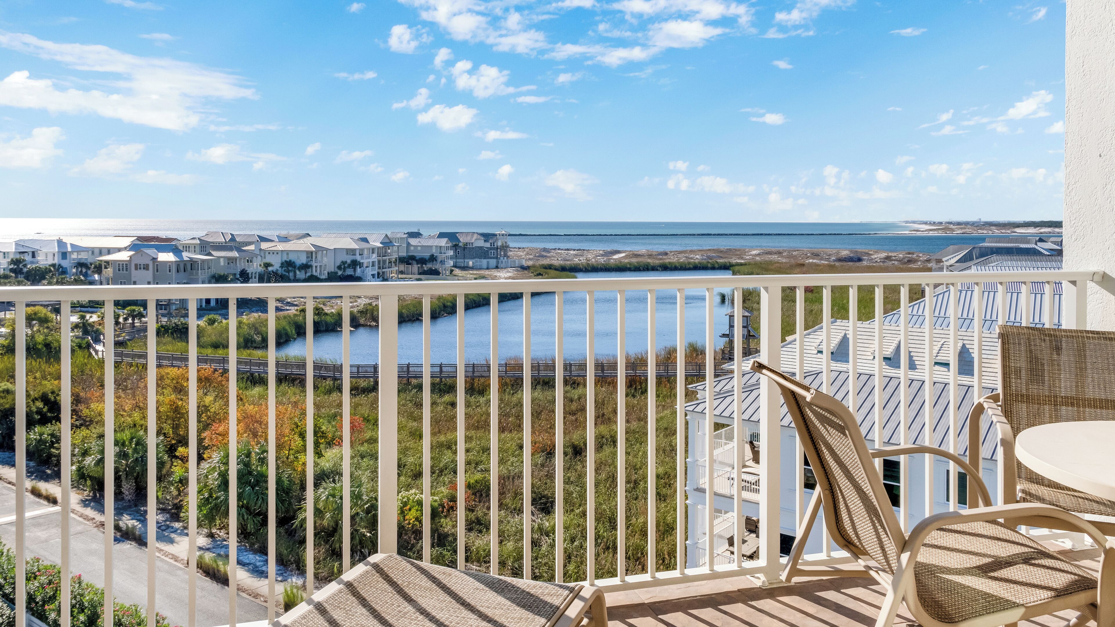 A balcony with wicker furniture overlooking a coastal view, including a body of water and distant buildings.