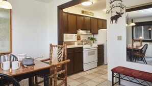 A compact kitchen with wooden cabinets, a white stove, and a microwave. There is a dining area with a wooden table and chairs, and a red bench. A sign on the wall reads "WELCOME TO THE LODGE." - JHRL - Tensleep B14, Cozy condo with skier shuttle access (Teton Village)
