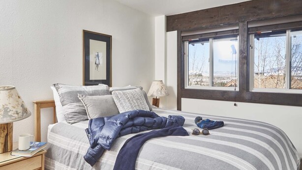 A bedroom with a large bed, a window with a view, a framed picture on the wall, and a lamp on the nightstand. - JHRL - Tensleep B14, Cozy condo with skier shuttle access (Teton Village)
