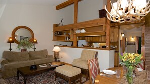 Un salon chaleureux avec un canapé, un fauteuil, une table basse et un coin repas avec une table mise pour deux personnes.