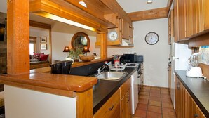 Une cuisine avec des meubles de rangement en bois, un plan de travail noir, un évier, un four à micro-ondes et une horloge murale.