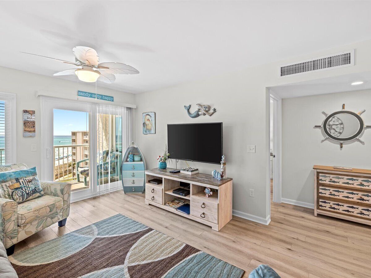 A living room with a TV, wooden entertainment unit, and a view of the sea through large windows.