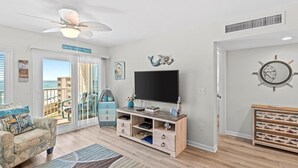 Een woonkamer met een televisie, een houten tv-meubel en uitzicht op zee door grote ramen.