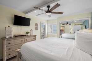 A bedroom with a large bed, a dresser, a flat-screen TV, a ceiling fan, and a mirror.