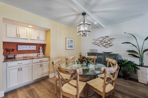 A dining area with a glass table surrounded by wooden chairs, white cabinetry, and a chandelier.