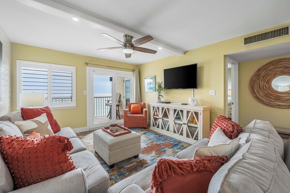 A living room with a sofa set, ottoman, and a television on a stand.