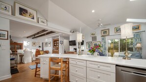 Una cocina amplia con armarios blancos, una mesa de comedor de madera y sillas. Cuenta con horno empotrado y un gran ventanal con cortinas.
