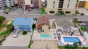 Un barrio residencial con una casa grande azul, una casa más pequeña con piscina, y un hotel Red Tree Inn al fondo.