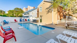 Un patio trasero con piscina, sillones de descanso y una pequeña terraza.