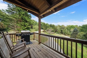 A wooden deck with a barbecue grill and seating, overlooking a forested landscape.