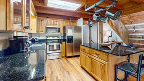 A kitchen with wooden cabinets, stainless steel appliances, a granite countertop, and hanging pots. - A Sunrise Summit - 4BR, 3BA - Hot Tub, Pets (Seven Devils)
