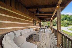 Un espacio de estar al aire libre techado con sofá y mesa, vigas de madera y vistas del paisaje circundante.