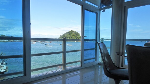 A room with large windows offering a view of the sea and a distant island. - Agua Sol Villa (Taboga)