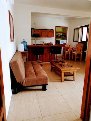 A living room with a sofa, a wooden coffee table, and a kitchen area with cabinets and a microwave. - Spacious Apartment in Central Oaxaca · Patio & Private Garage (Oaxaca)