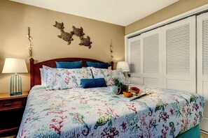 Une chambre à coucher avec une couvre-lit à motifs floraux, deux lampes de chevet, une tête de lit en bois et un élément décoratif mural.