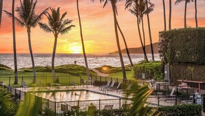 A pool area with lounge chairs and a view of the ocean at sunset. - Beachfront Bliss , cancellation 8/15 to 8/22. need a dry place in the storm? (Kihei)