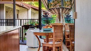 A dining area with a table set for two, a laptop, and a bowl of fruit. - Beachfront Bliss , cancellation 8/15 to 8/22. need a dry place in the storm? (Kihei)