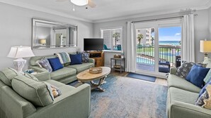 A living room with a ceiling fan, a television, and a view of the ocean through large sliding doors. - 209-Tranquil Relaxation on Florida's Gulf Coast, includes FREE Beach Service (Destin)