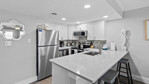A modern kitchen with white cabinetry, stainless steel appliances, and a central island with bar stools. - 209-Tranquil Relaxation on Florida's Gulf Coast, includes FREE Beach Service (Destin)