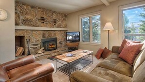 A cozy living room with a stone fireplace, leather sofa, and a television. - JHRL - Rendezvous B3, Comfortable Slope-side Condo, Hot tub next door (Teton Village)