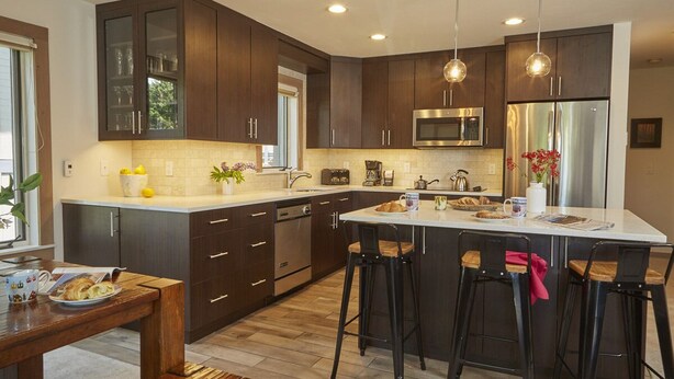 A modern kitchen with dark wood cabinets, stainless steel appliances, and a central island with bar stools. - JHRL - Rendezvous B3, Comfortable Slope-side Condo, Hot tub next door (Teton Village)