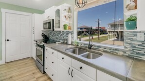 Una cocina moderna con armarios blancos, un lavamanos doble, un microondas y vistas a una casa a través de un ventanal grande.
