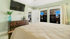 Un dormitorio con una cama grande, un aparador, un televisor montado en la pared y una puerta corrediza que da a un balcón.