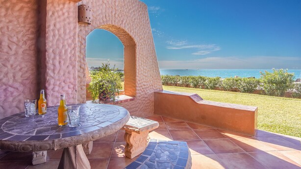 An outdoor patio with a stone table, a potted plant, and a view of the sea.