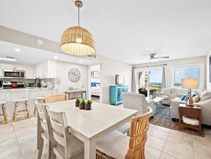 A modern kitchen with white cabinets, a dining area with a white table and chairs, and a living room with a sofa and a TV.