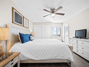 A bedroom with a bed, a ceiling fan, a TV, and a dresser.