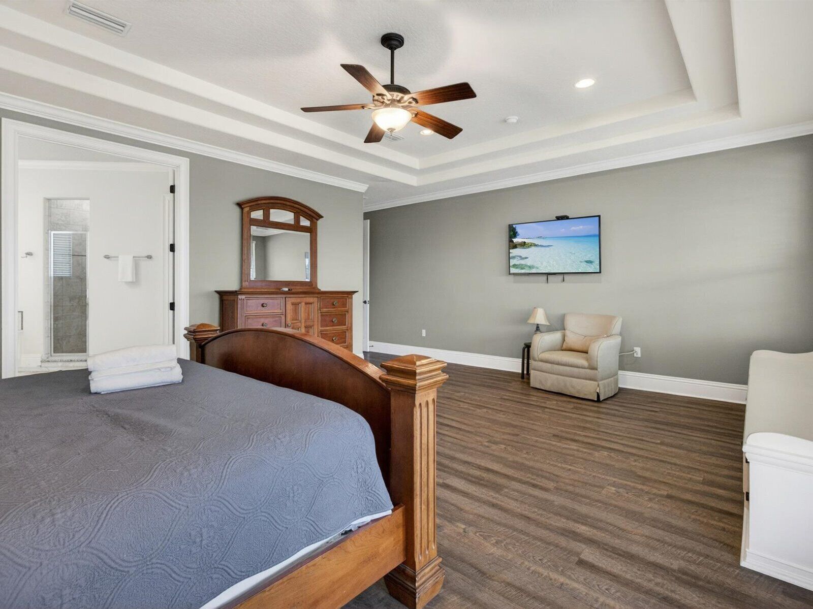Une chambre à coucher comprenant un lit, un ventilateur de plafond, une commode, une chaise, un téléviseur et une douche.