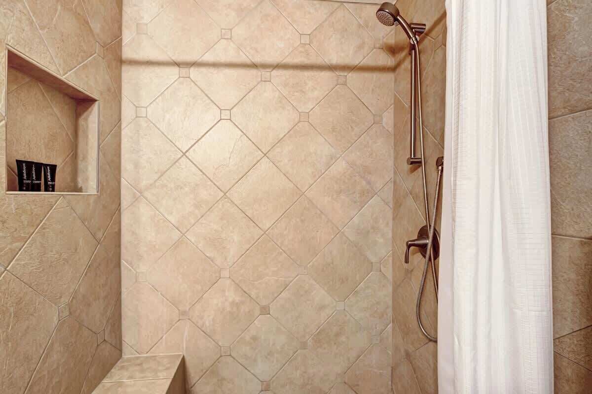 A shower area with a hexagonal tile pattern, a built-in shelf with toiletries, and a showerhead.