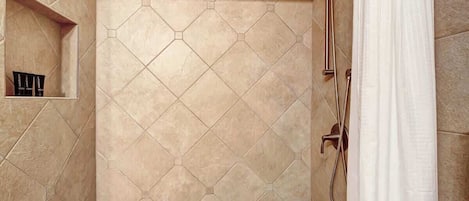 A shower area with a hexagonal tile pattern, a built-in shelf with toiletries, and a showerhead.