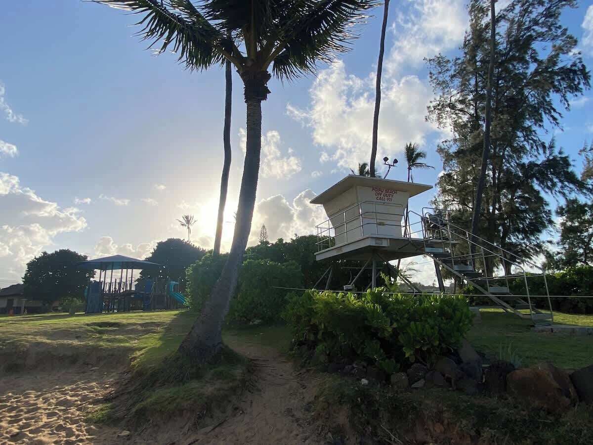 A lifeguard tower with a sign, surrounded by trees and a playground.