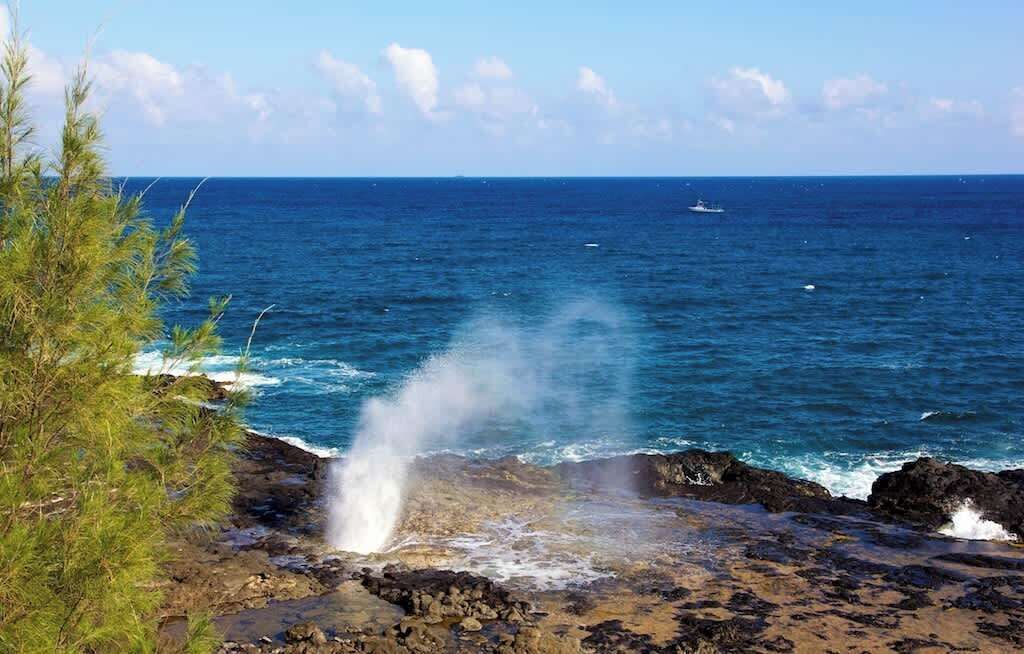 A coastal scene with a rocky shoreline, ocean waves, and a distant boat.