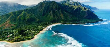 An aerial view of a coastal area with a mountain, clear blue waters, and a beach.