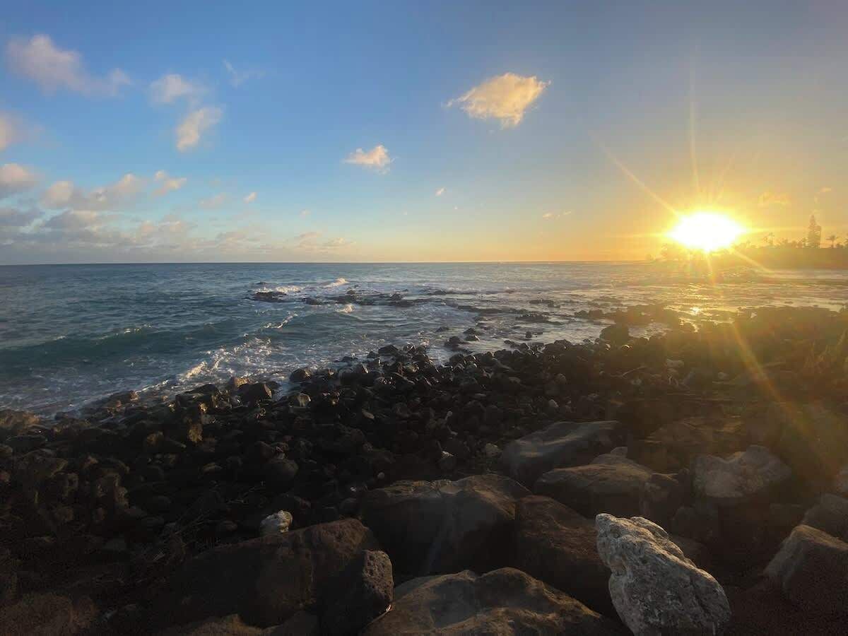 Una costa rocosa con el sol poniéndose sobre el océano.
